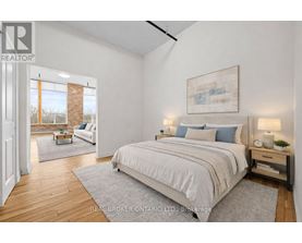 A bedroom with a large bed, a nightstand, and a window with a view of a tree.