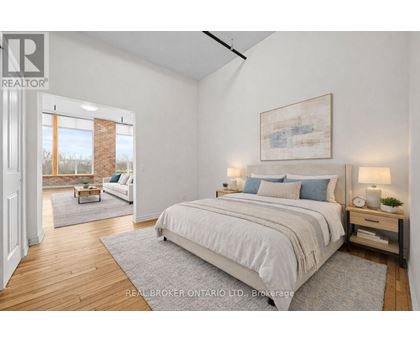 A bedroom with a large bed, a nightstand, and a window with a view of a tree.