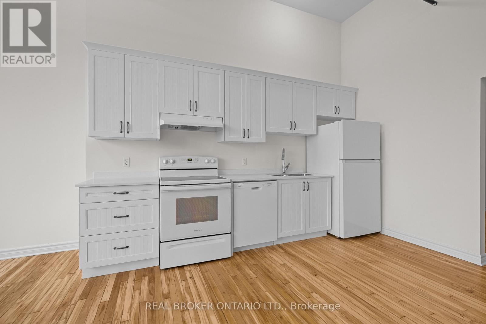 A kitchen with white cabinets and appliances on a wood floor.