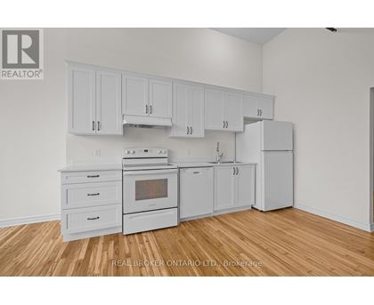 A kitchen with white cabinets and appliances on a wood floor.