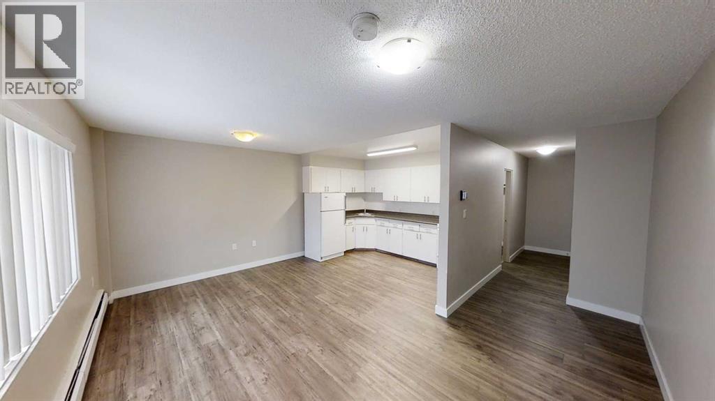 A spacious room with wooden flooring and a kitchenette in the background.