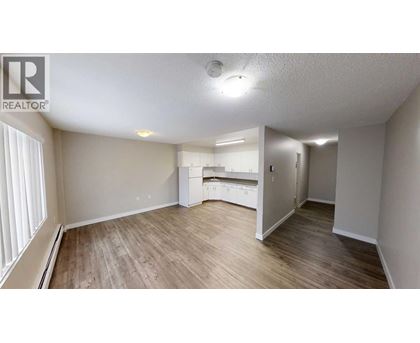 A spacious room with wooden flooring and a kitchenette in the background.