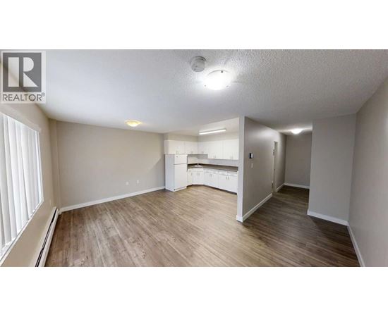 A spacious room with wooden flooring and a kitchenette in the background.