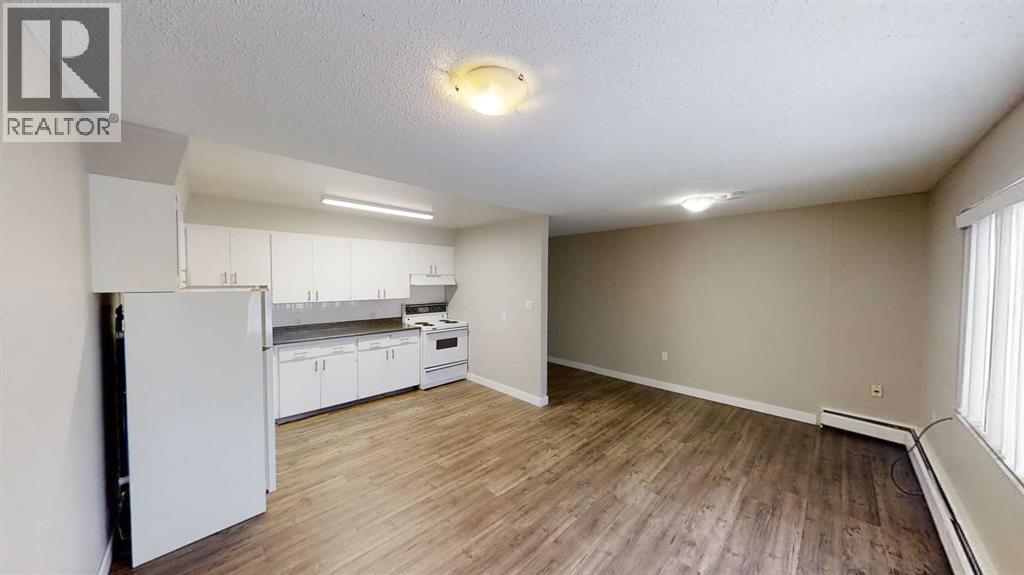 A well-lit, empty room with a white refrigerator and wooden flooring.