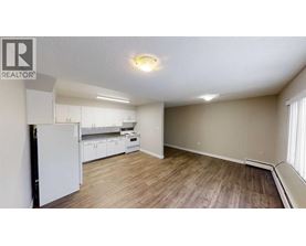A well-lit, empty room with a white refrigerator and wooden flooring.