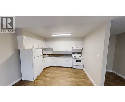 A kitchen with white appliances and cabinets in a room with wooden floors.