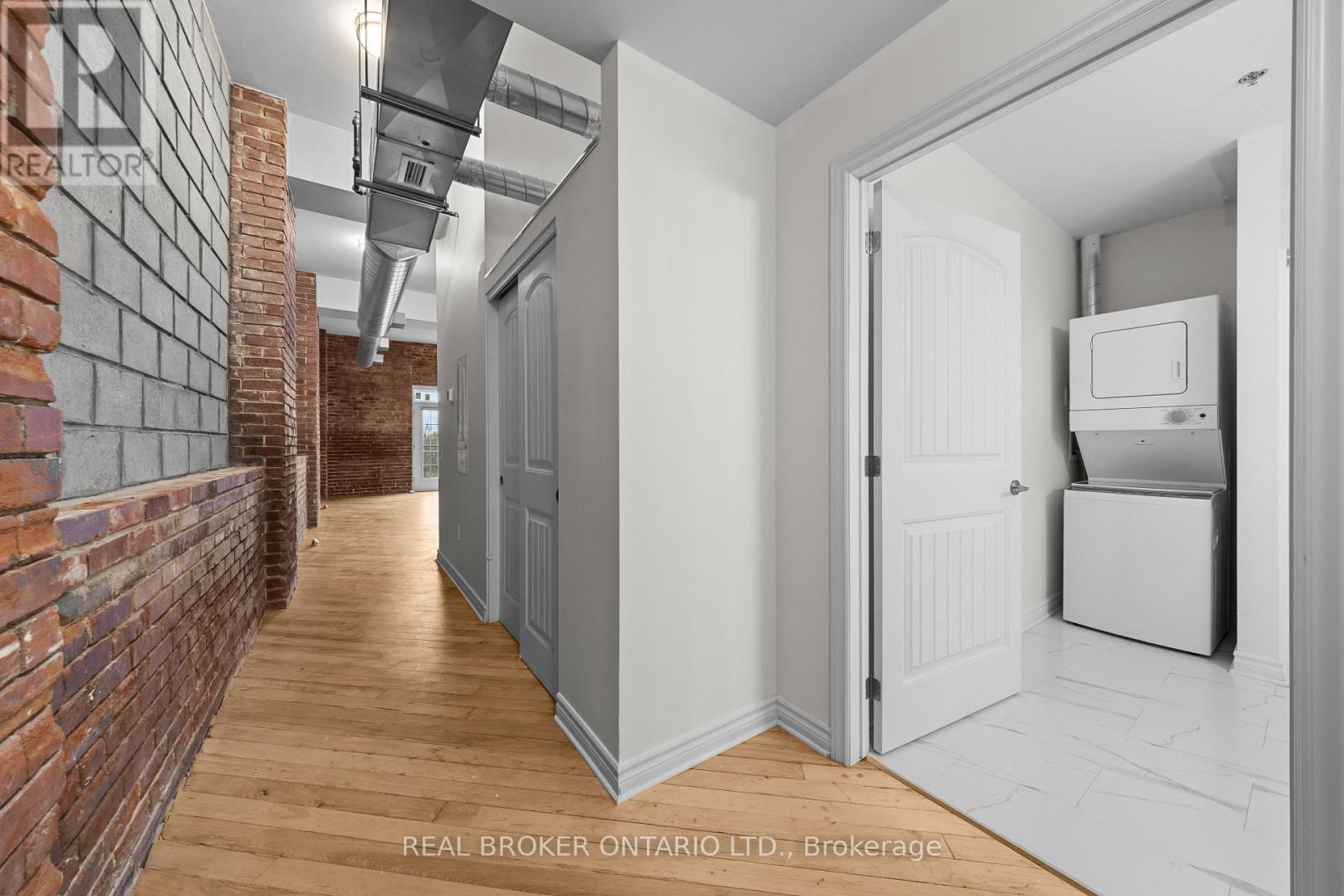 A hallway with a brick wall on the left and a white door on the right.