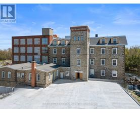 A large building with a flat roof and a chimney is surrounded by a parking lot.