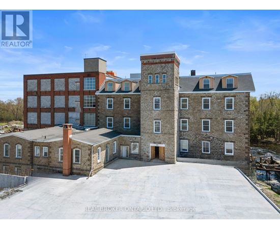 A large building with a flat roof and a chimney is surrounded by a parking lot.