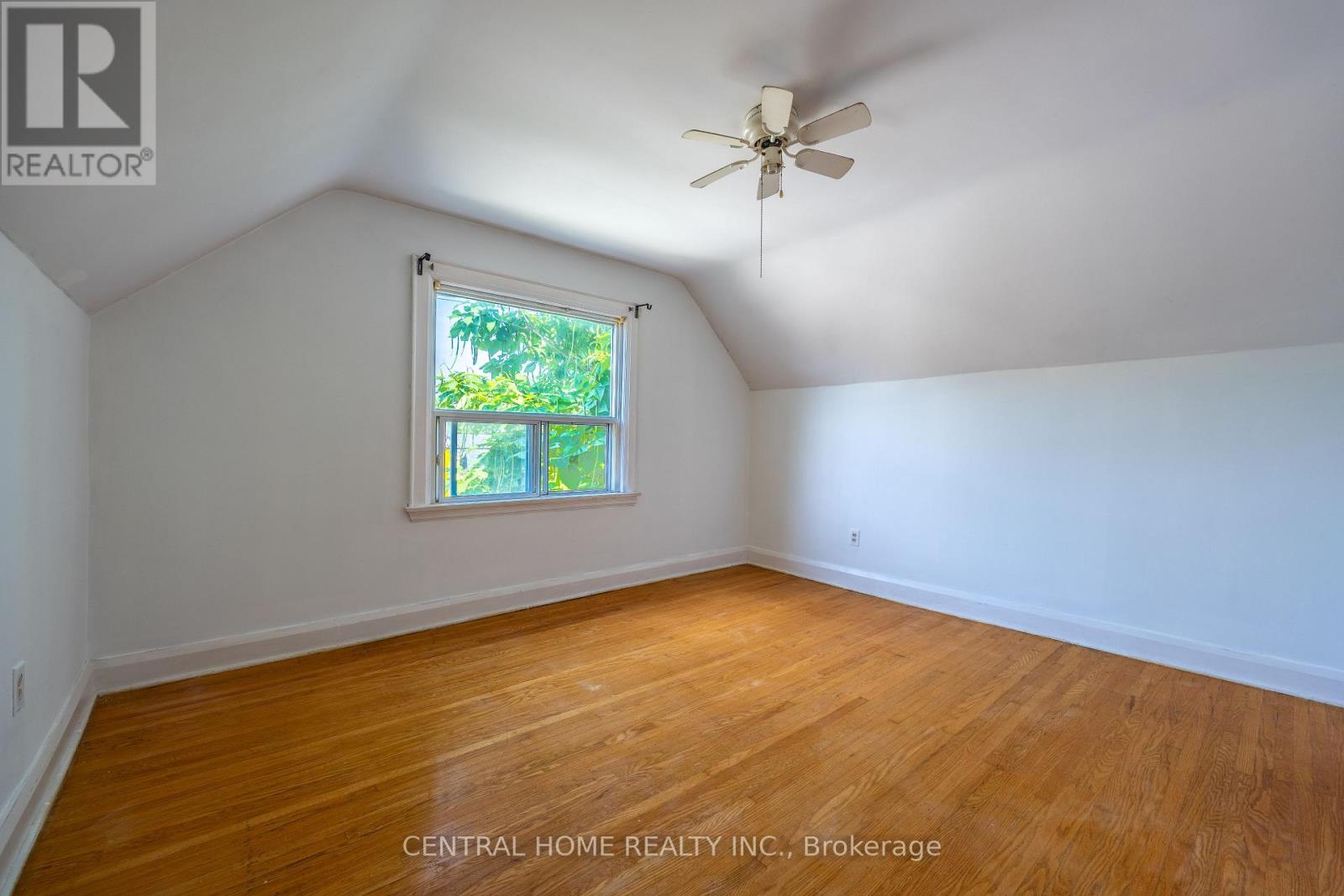 A room with a ceiling fan and a window with a view of trees.