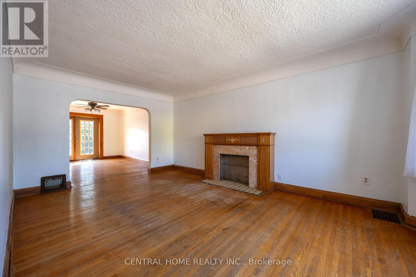 A large empty room with a fireplace and wood flooring.