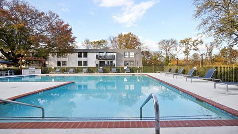 A large outdoor swimming pool with a red brick border and a metal ladder.