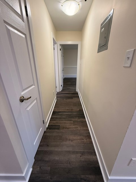 A long hallway with a white door on the left and a light switch on the wall.