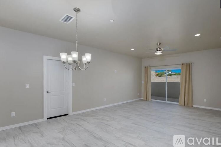 A spacious room with a chandelier, a door, and a window with curtains.