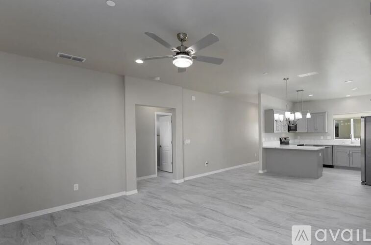 A spacious room with a ceiling fan and a kitchen area in the background.