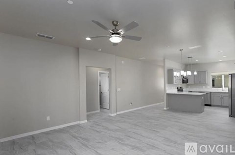 A spacious room with a ceiling fan and a kitchen area in the background.