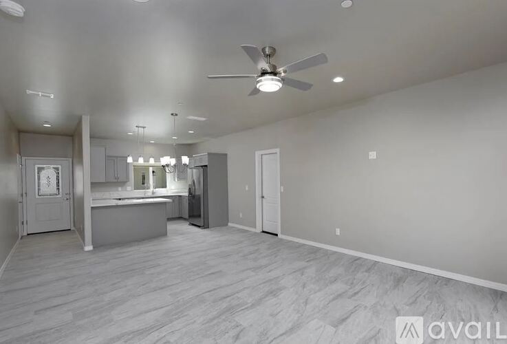 A spacious room with a ceiling fan and a kitchen area in the background.
