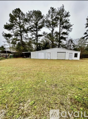 A large white building sits in a grassy field with trees in the background.