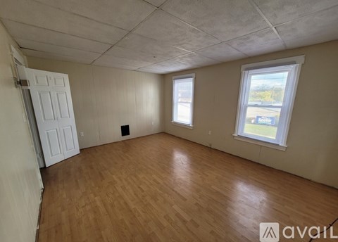 A room with wooden flooring and a window showing a view of a parking lot.