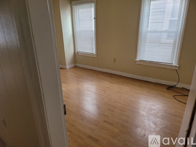 A room with wooden flooring and two windows with blinds.