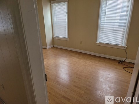 A room with wooden flooring and two windows with blinds.