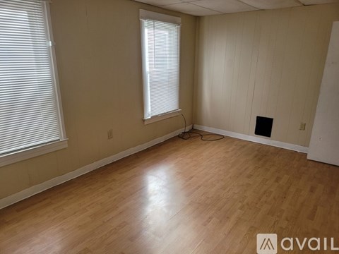 A room with wooden flooring and two windows.