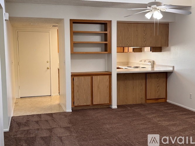 A room with a white door, a fan, and a kitchenette with a stove and cabinets.