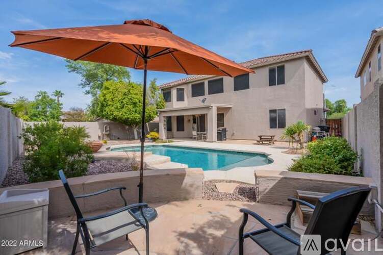 A pool with a patio and a chair with an orange umbrella.