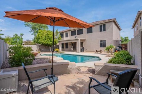 A pool with a patio and a chair with an orange umbrella.