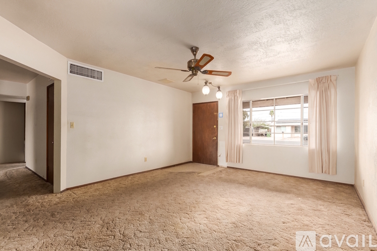 A room with a carpeted floor, a ceiling fan, and a window with curtains.