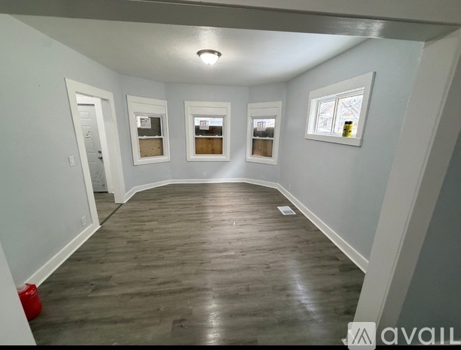 A room with wooden flooring and three windows.