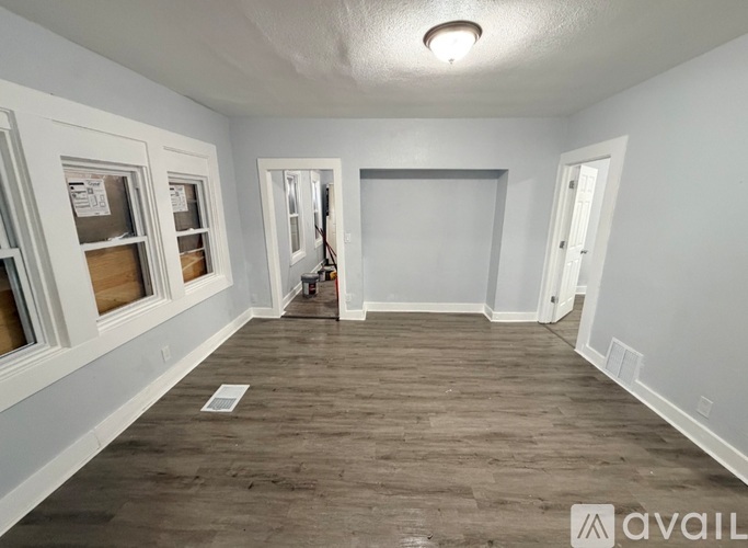 A room with wooden flooring and white walls, with a window on the left and a door on the right.