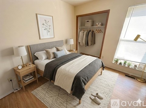 A bedroom with a large bed, a nightstand with a lamp, and a window with a view of plants outside.