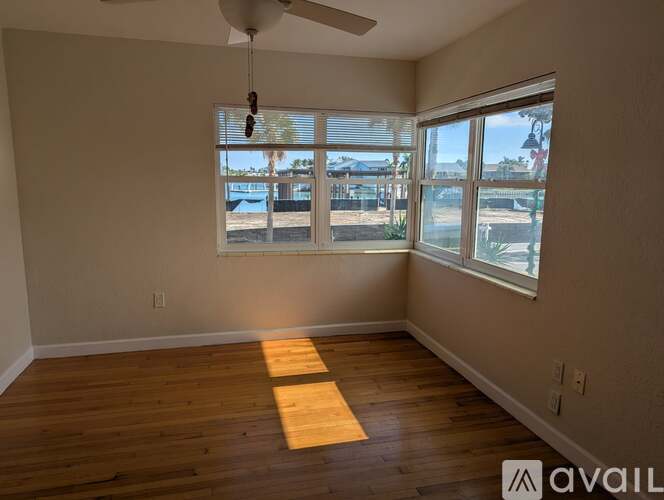 A room with wooden flooring and a window overlooking a fenced area.