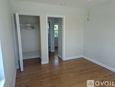 A room with wooden floors and a white wall with a doorway leading to another room.