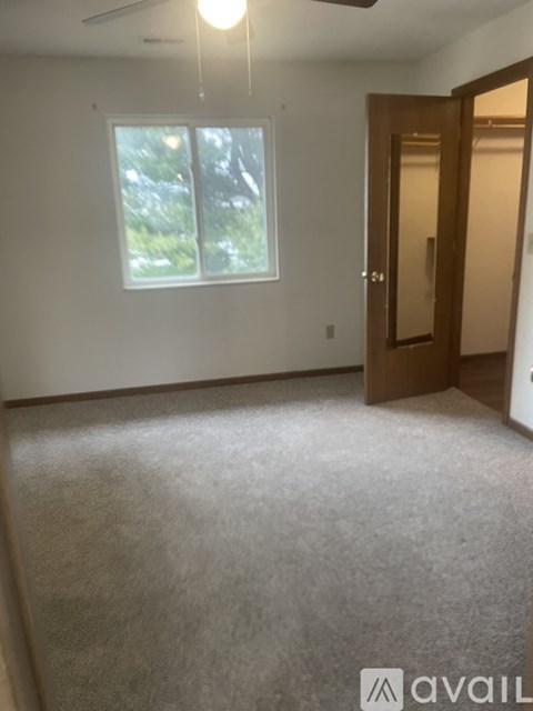 A room with a carpeted floor, a ceiling fan, and a door leading to another room.