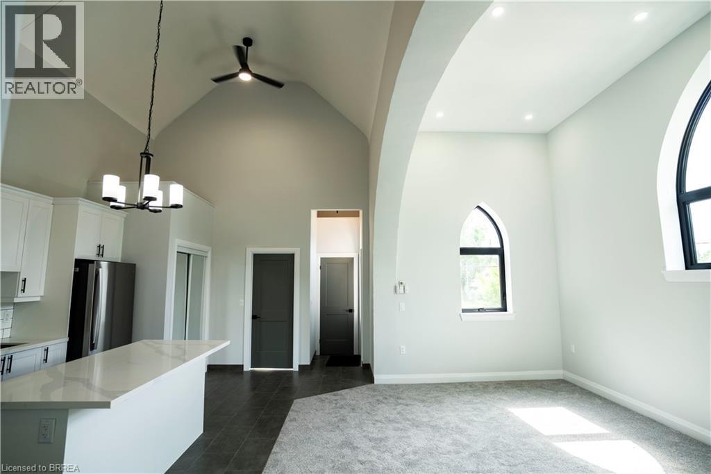 A spacious, empty room with a kitchen area to the left and a doorway leading to another room.