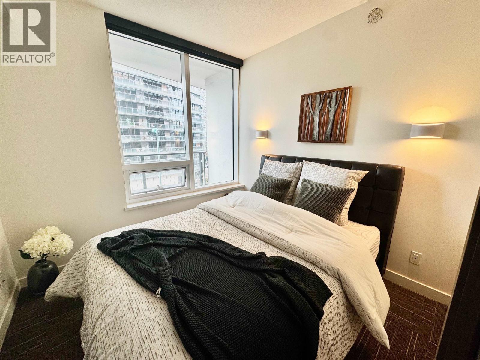 A bedroom with a large bed and a window overlooking a cityscape.
