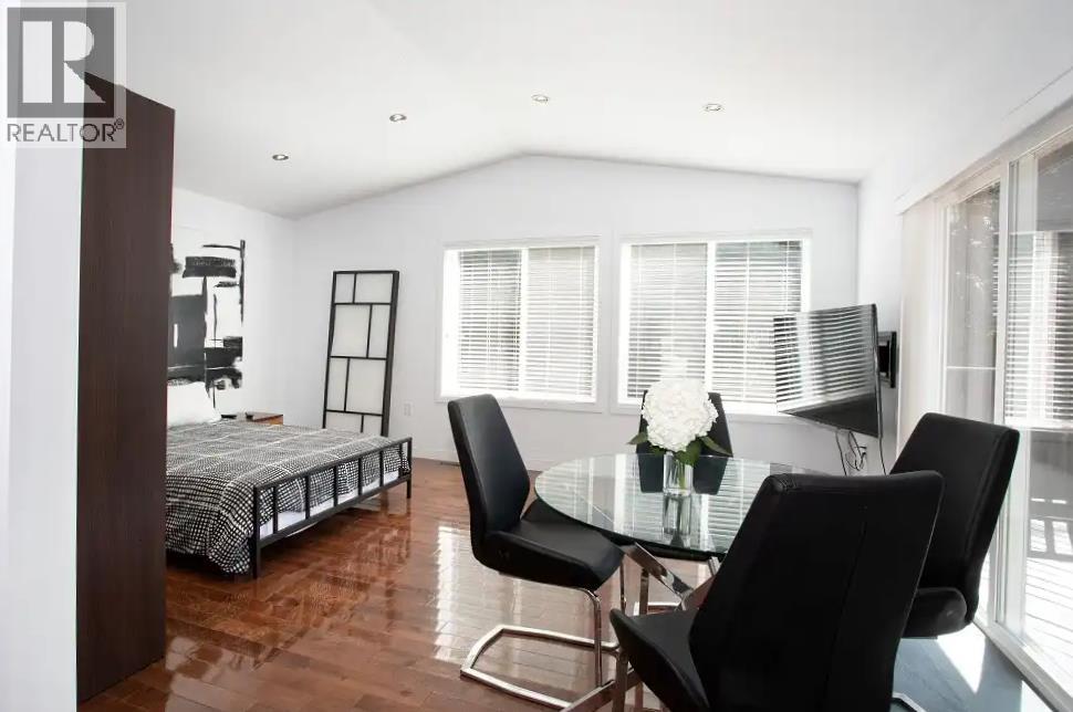 A bedroom with a bed, a table and chairs, and a window with blinds.