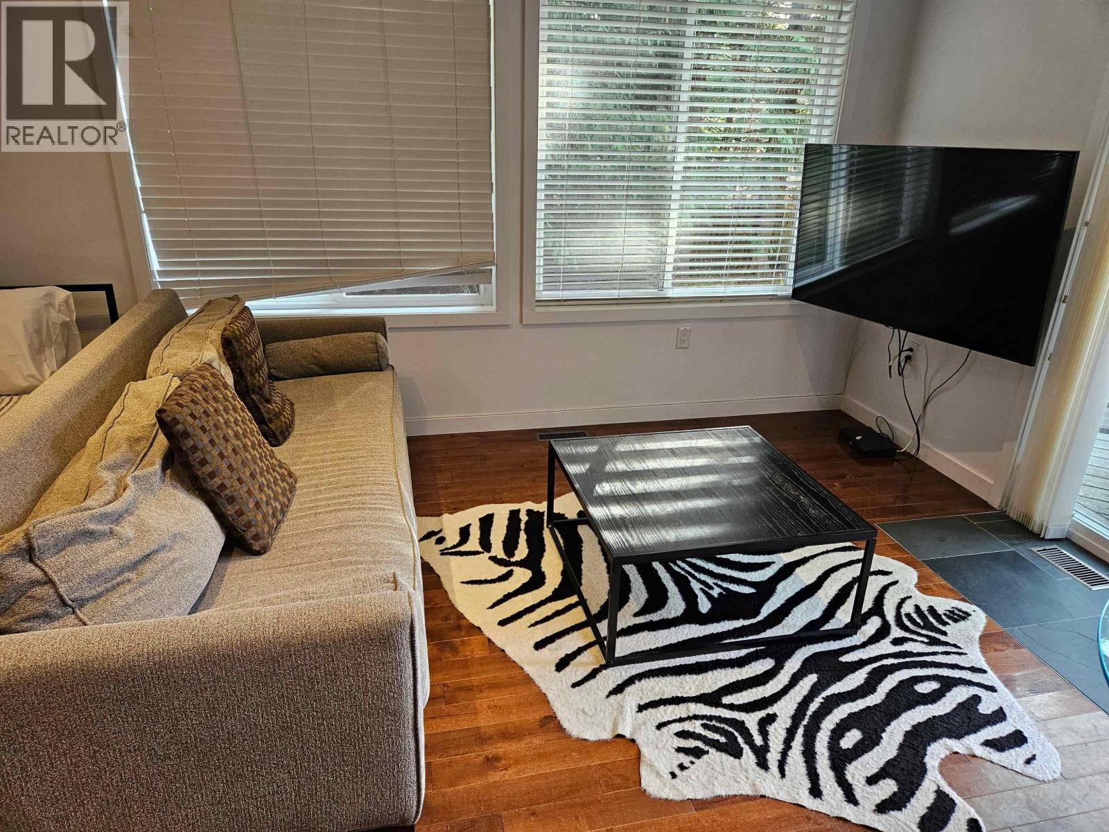 A living room with a grey couch, a zebra rug and a black television.