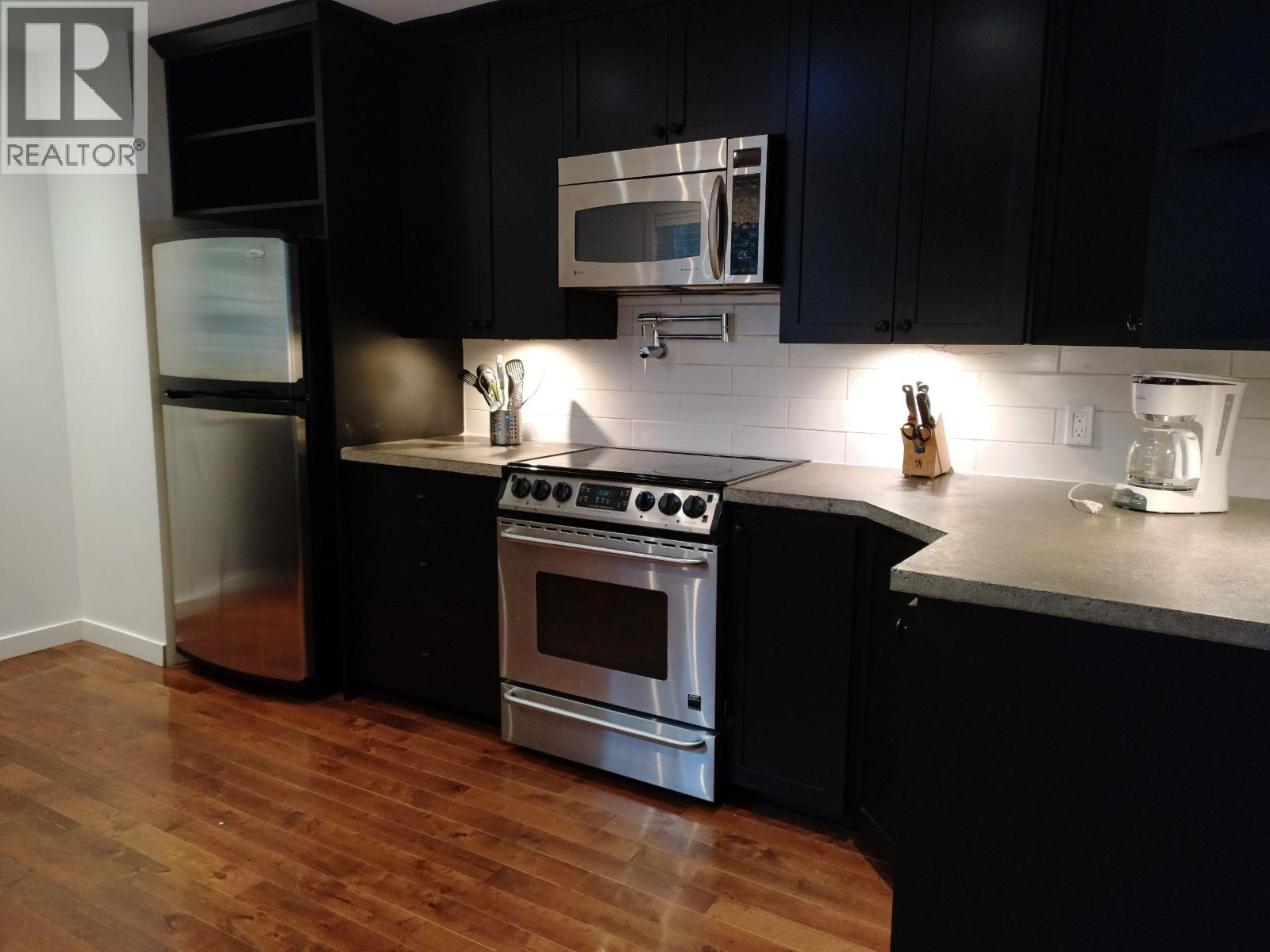 A modern kitchen with black cabinets and stainless steel appliances.