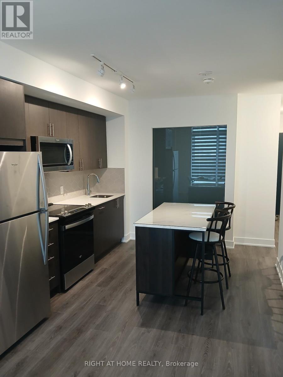 A kitchen with a refrigerator, microwave, and a counter with a bar stool.