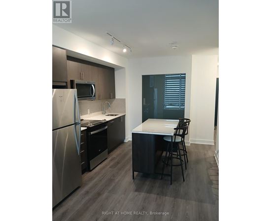 A kitchen with a refrigerator, microwave, and a counter with a bar stool.