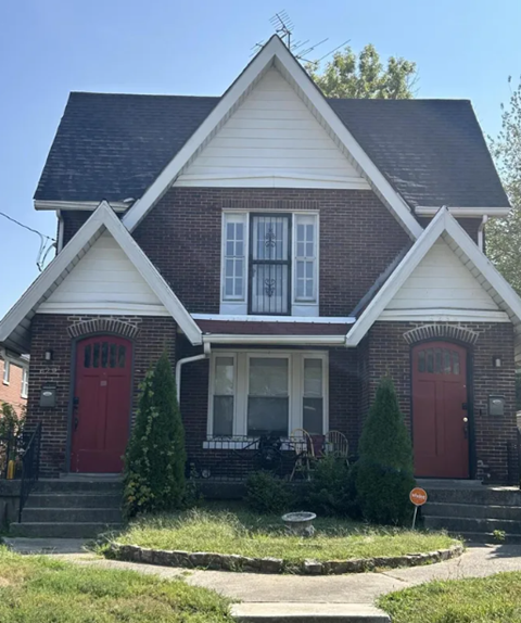A brick house with a red door and a white window.