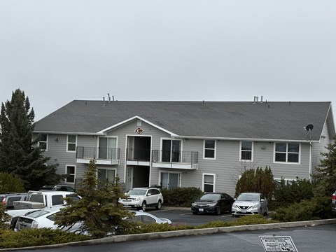 A grey apartment building with cars parked in front.
