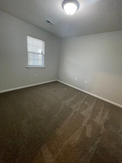 A room with a carpeted floor and a window with blinds.