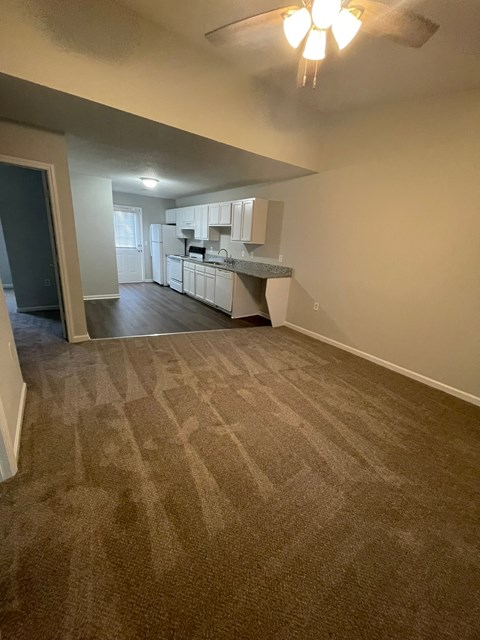 A room with a carpeted floor and a kitchen in the background.