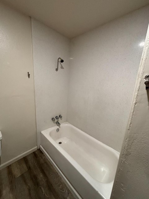 A white bathtub in a small bathroom with a toilet and a shower head.