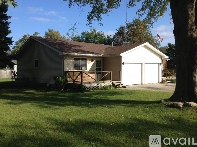 A house with a brown roof and a white garage door is surrounded by a grassy lawn.