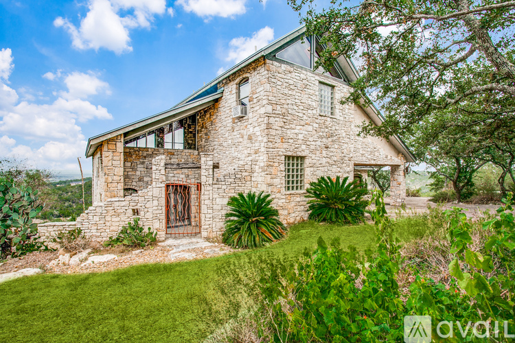 A house with a stone facade and a metal gate is surrounded by greenery.
